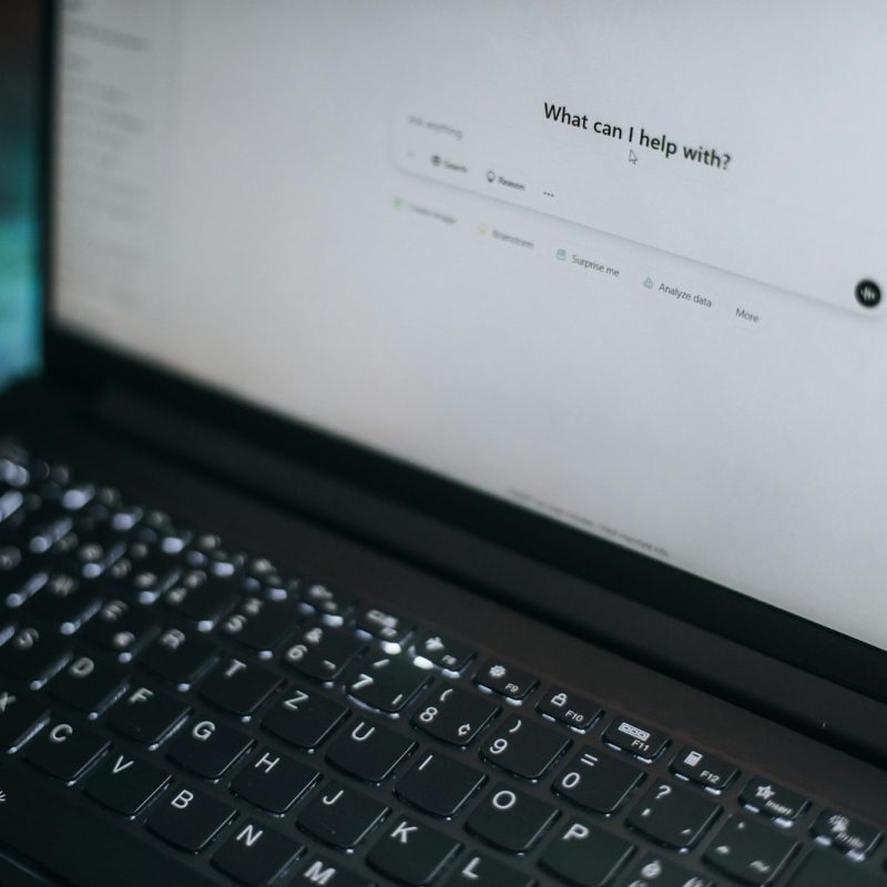 A laptop displays "what can i help with?"